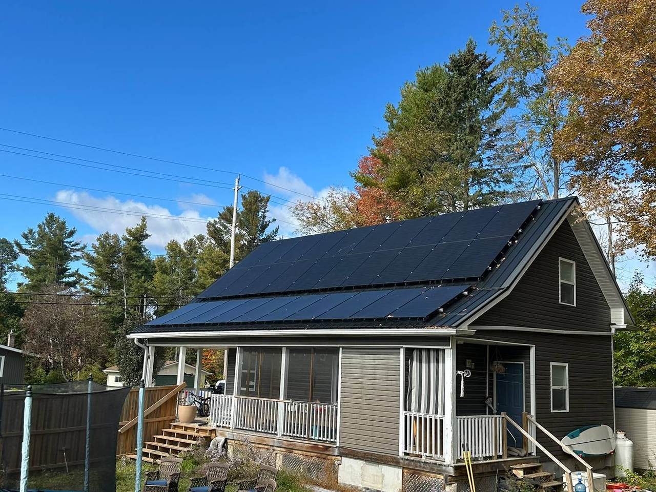 A full roof of black solar panels on a cottage under a blue sky