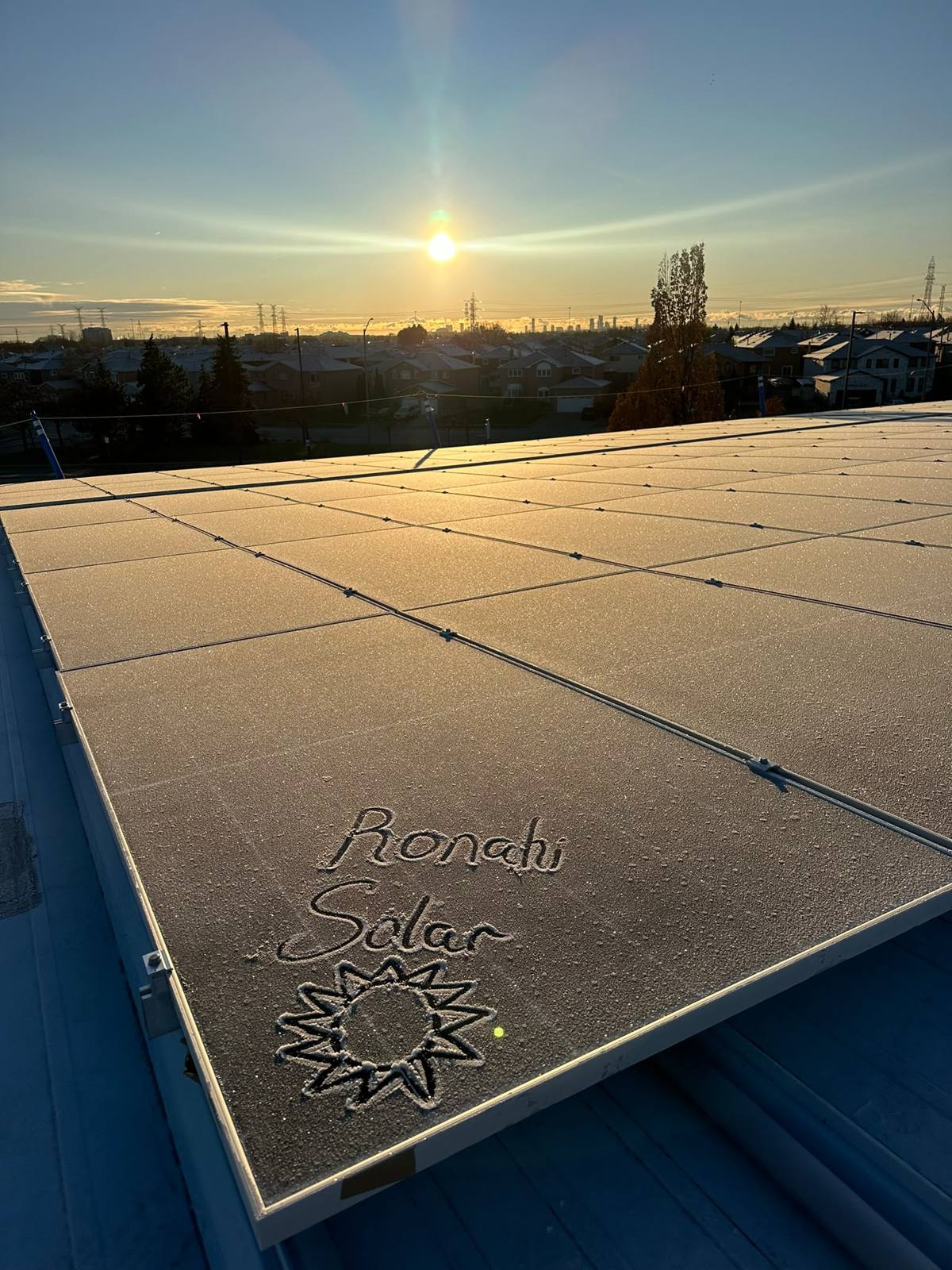 Ronahi Solar and a sun drawn in the frost on a commercial solar array at sunrise